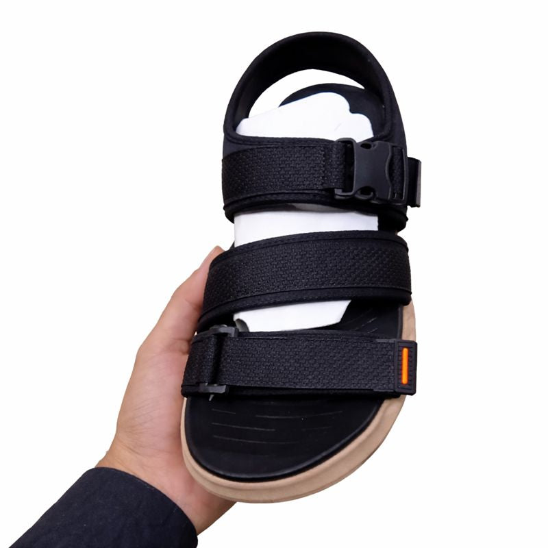 Black orthopedic sandal with beige sole held by a hand front side view on a white background