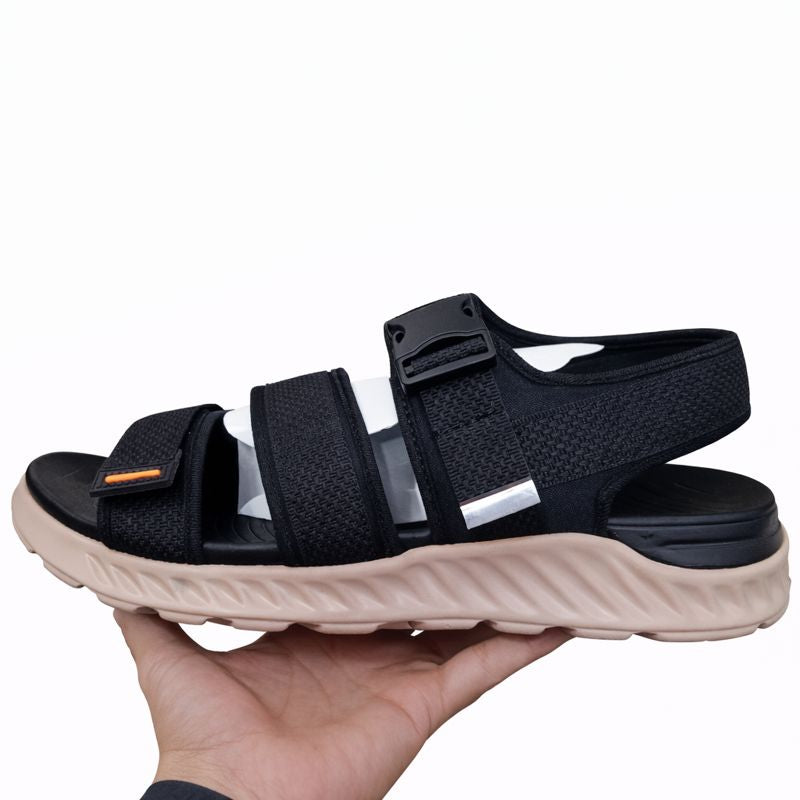 Black sandal with a beige sole held in a hand against a white background