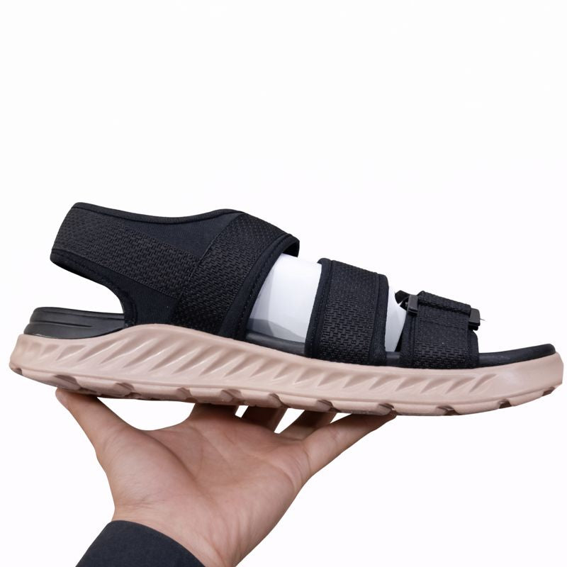Black sandal with beige sole held by a hand left side view on a white background