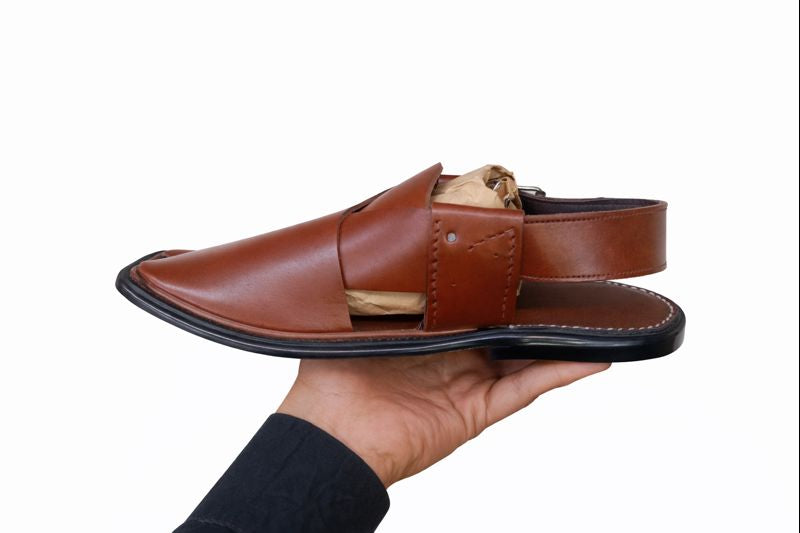 Brown peshawari sandal left side view held in a hand against a white background