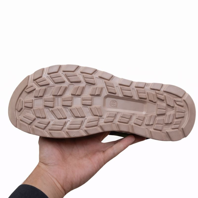 Close-up of a hand holding a beige sneaker sole with tread pattern on a white background