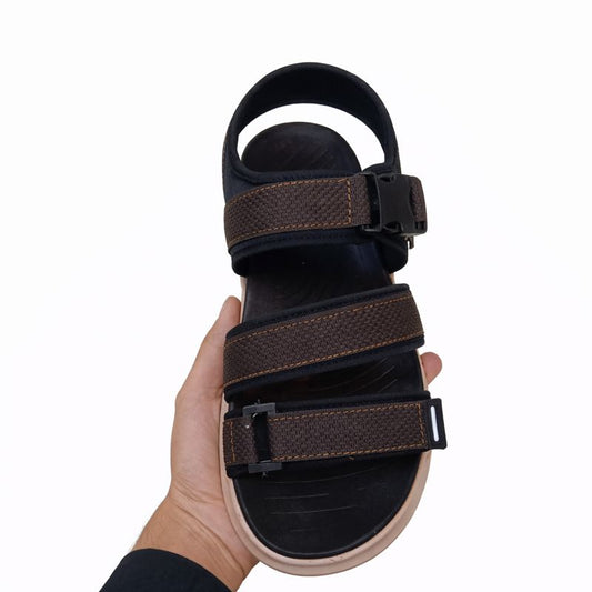 Hand holding a black and brown sandal with multiple straps  front view on a white background