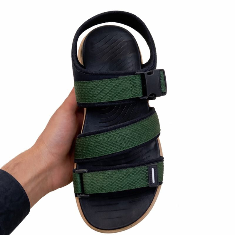 Hand holding a black and green sandal front view with a white background