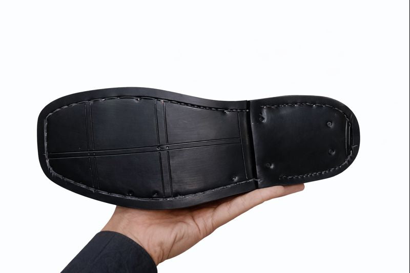 Black Sole with a hand holding it against a white background